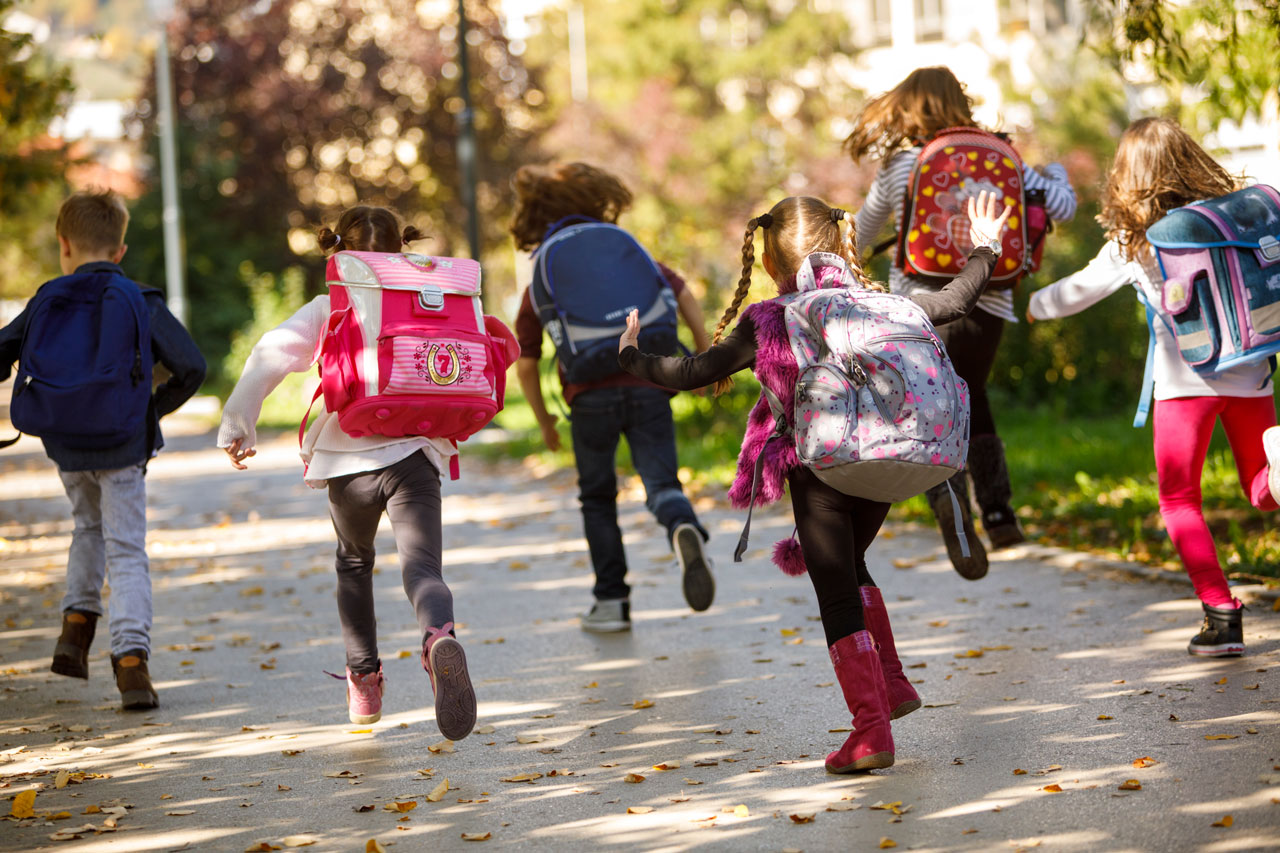 Zes rennende kinderen met rugzak op, gezien van achteren